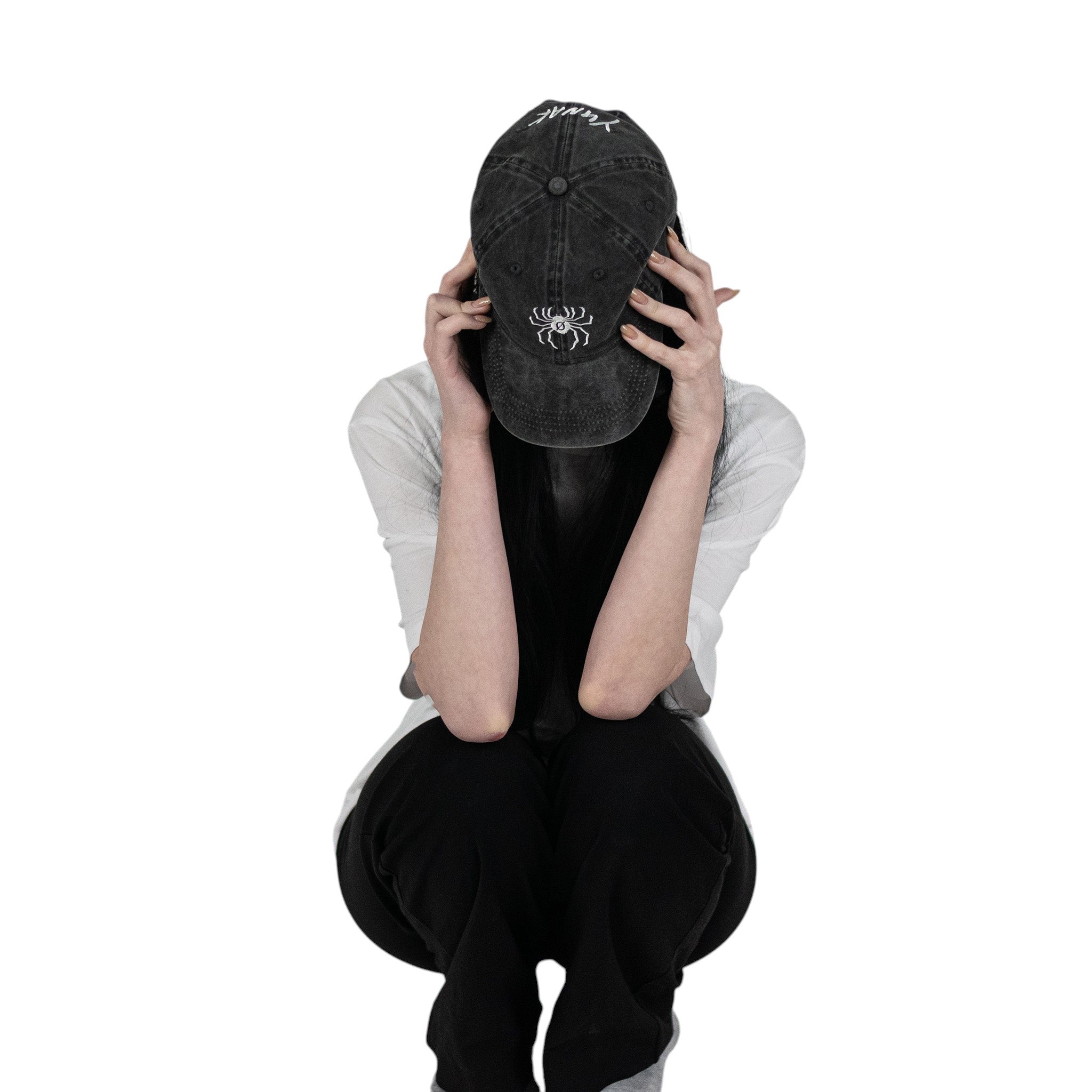 Person wearing a black vintage unstructured dad hat with embroidered white design of Chrollo spider from HunterxHunter on the front, squatting against a white background