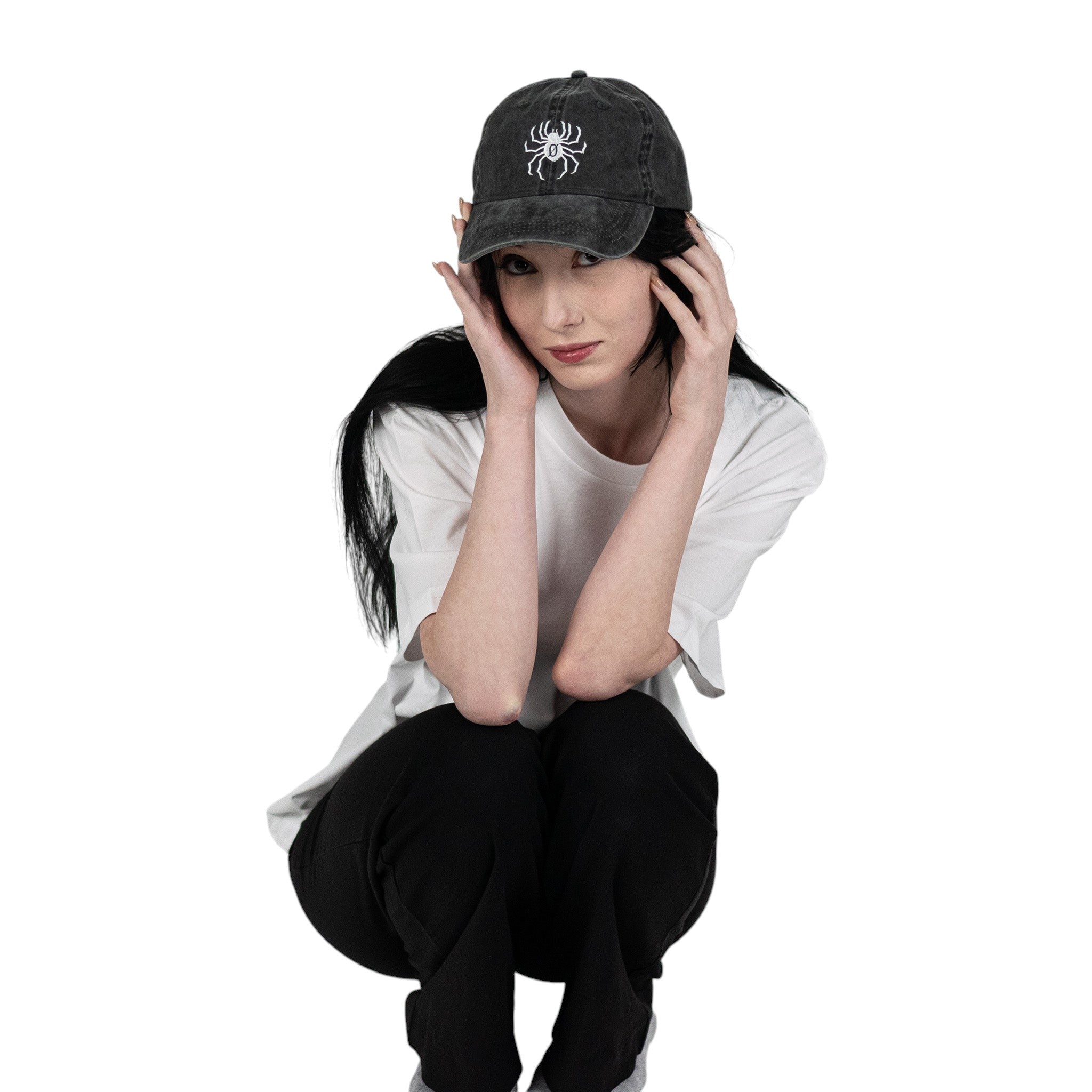 Person wearing a black vintage unstructured dad hat with embroidered white design of Chrollo spider from HunterxHunter on the front, squatting against a white background