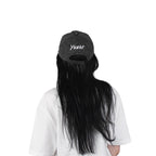 Person wearing a black vintage unstructured dad hat with embroidered white design of Yunak on the back standing against a white background