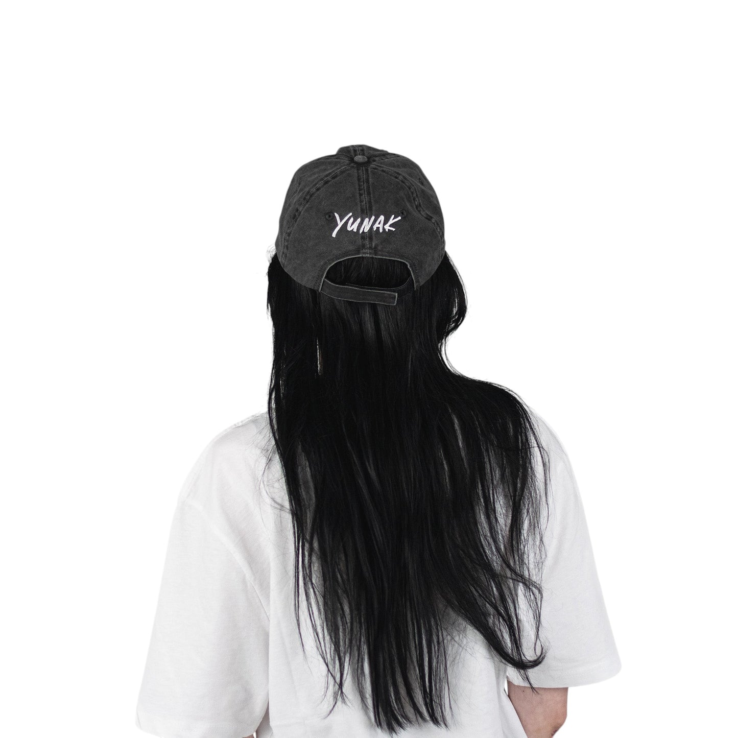 Person wearing a black vintage unstructured dad hat with embroidered white design of Yunak on the back standing against a white background