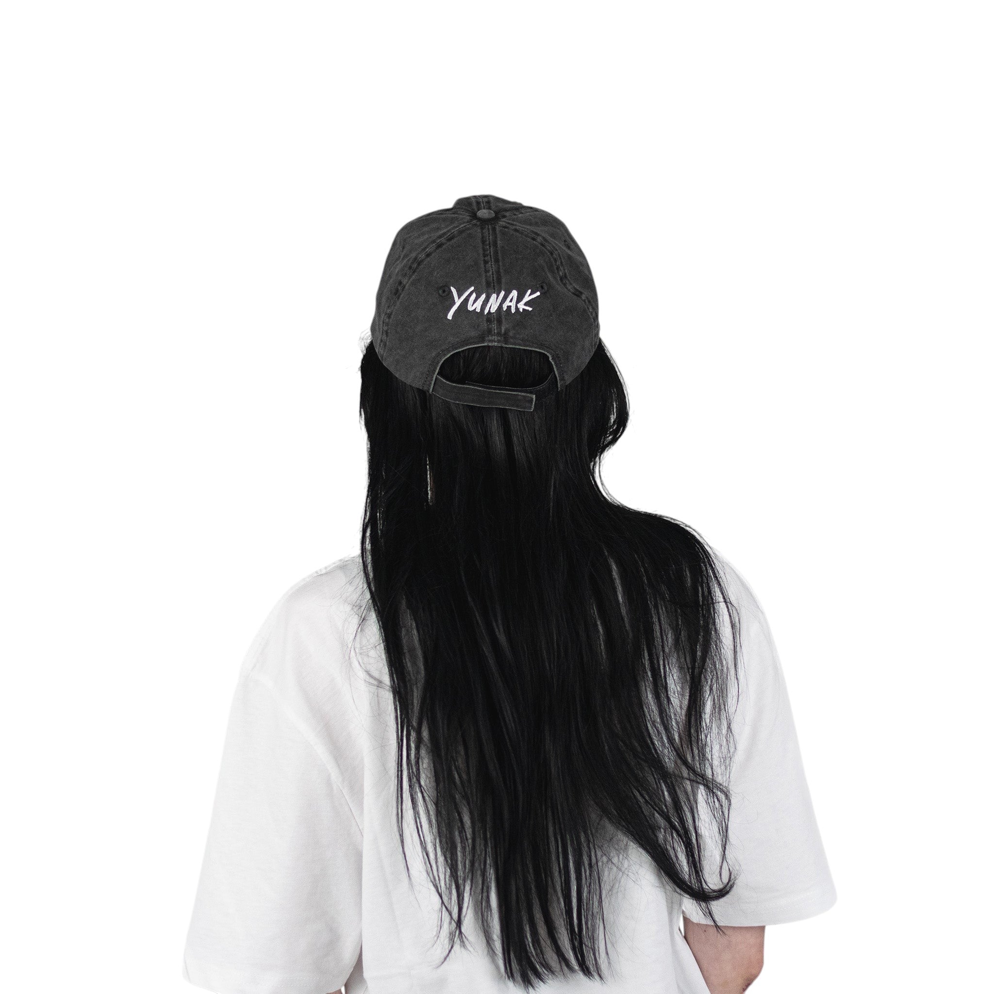 Person wearing a black vintage unstructured dad hat with embroidered white design of Yunak on the back standing against a white background