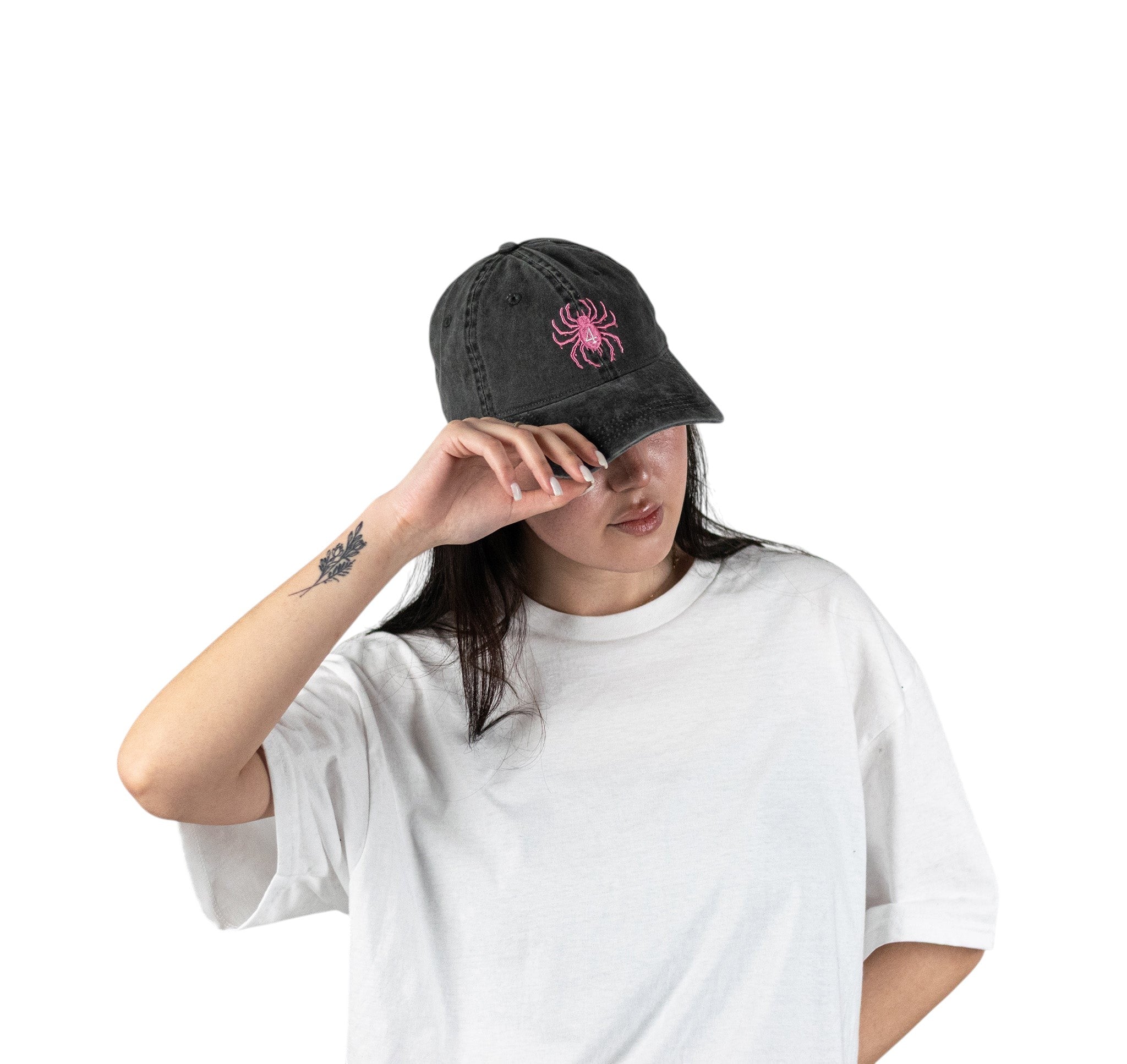 Person wearing a black vintage unstructured dad hat with embroidered pink design of Hisoka spider from HunterxHunter on the front, standing against a white background