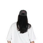 Person wearing a black vintage unstructured dad hat with embroidered pink design of Yunak on the back, standing against a white background