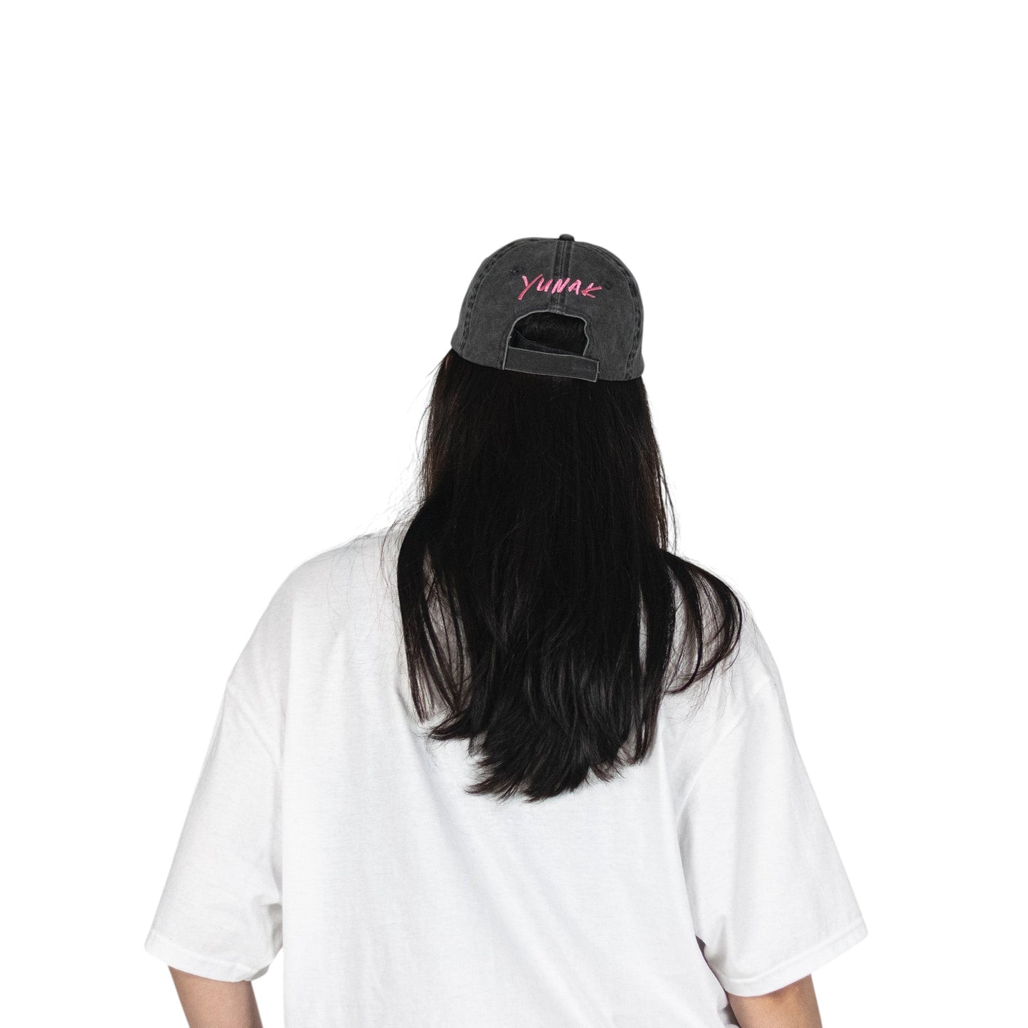 Person wearing a black vintage unstructured dad hat with embroidered pink design of Yunak on the back, standing against a white background
