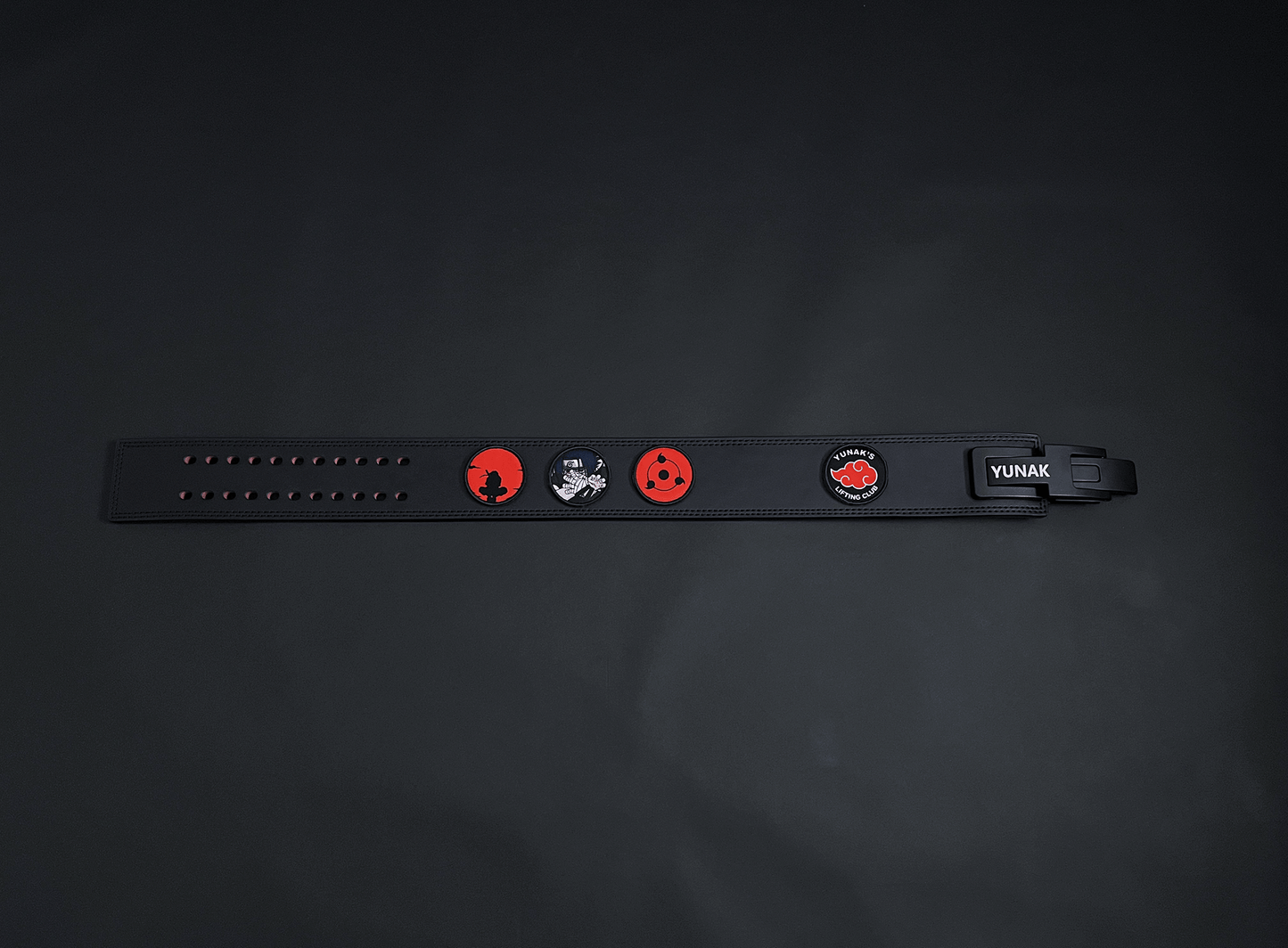 An anime powerlifting belt, 13mm thick and 4 inch wide. Featuring 4 embroidery patches inspired by the Akatsuki clan. First patch is Itachi bright red background, second is Sasuke, third is featuring the Sharingan and the fourth is a Yunak's Lifting Club patch. The photo is top down view of the belt.