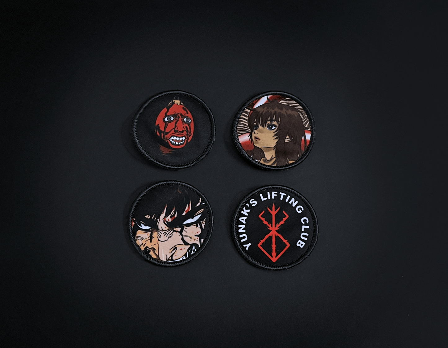 A photo of the 4 anime embroidery patches that come with this belt variation. First patch is behelit. Second patch is Casca, third is featuring Guts and the fourth is a Yunak's Lifting Club patch. The photo is top down view of the patches.