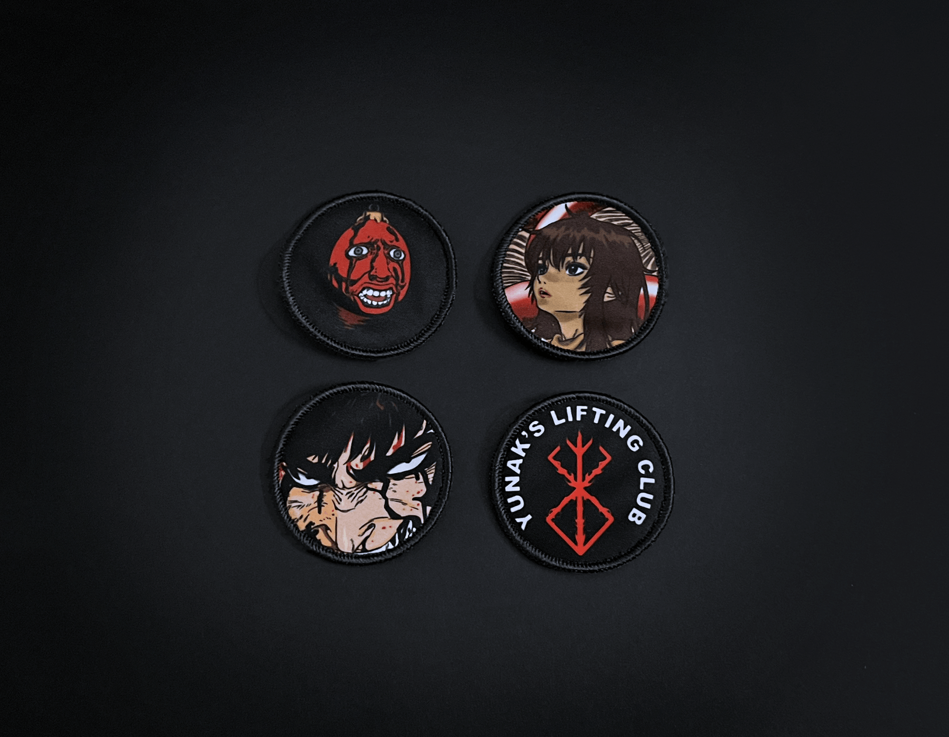 A photo of the 4 anime embroidery patches that come with this belt variation. First patch is behelit. Second patch is Casca, third is featuring Guts and the fourth is a Yunak's Lifting Club patch. The photo is top down view of the patches.