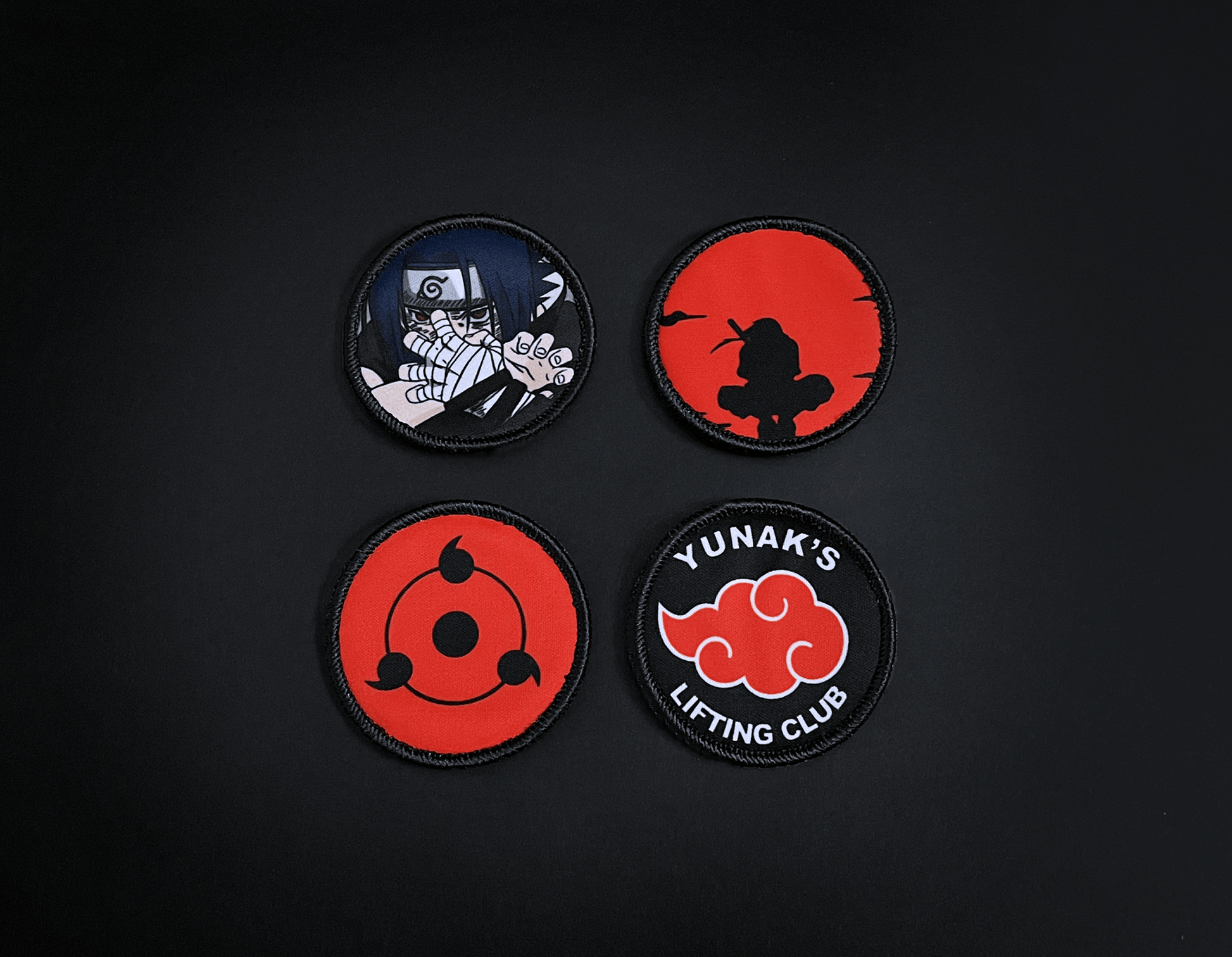 A photo of the 4 anime embroidery patches that come with this belt variation. First patch is Sasuke. Second patch is Itachi bright red background, third is featuring the Sharingan and the fourth is a Yunak's Lifting Club patch. The photo is top down view of the patches.