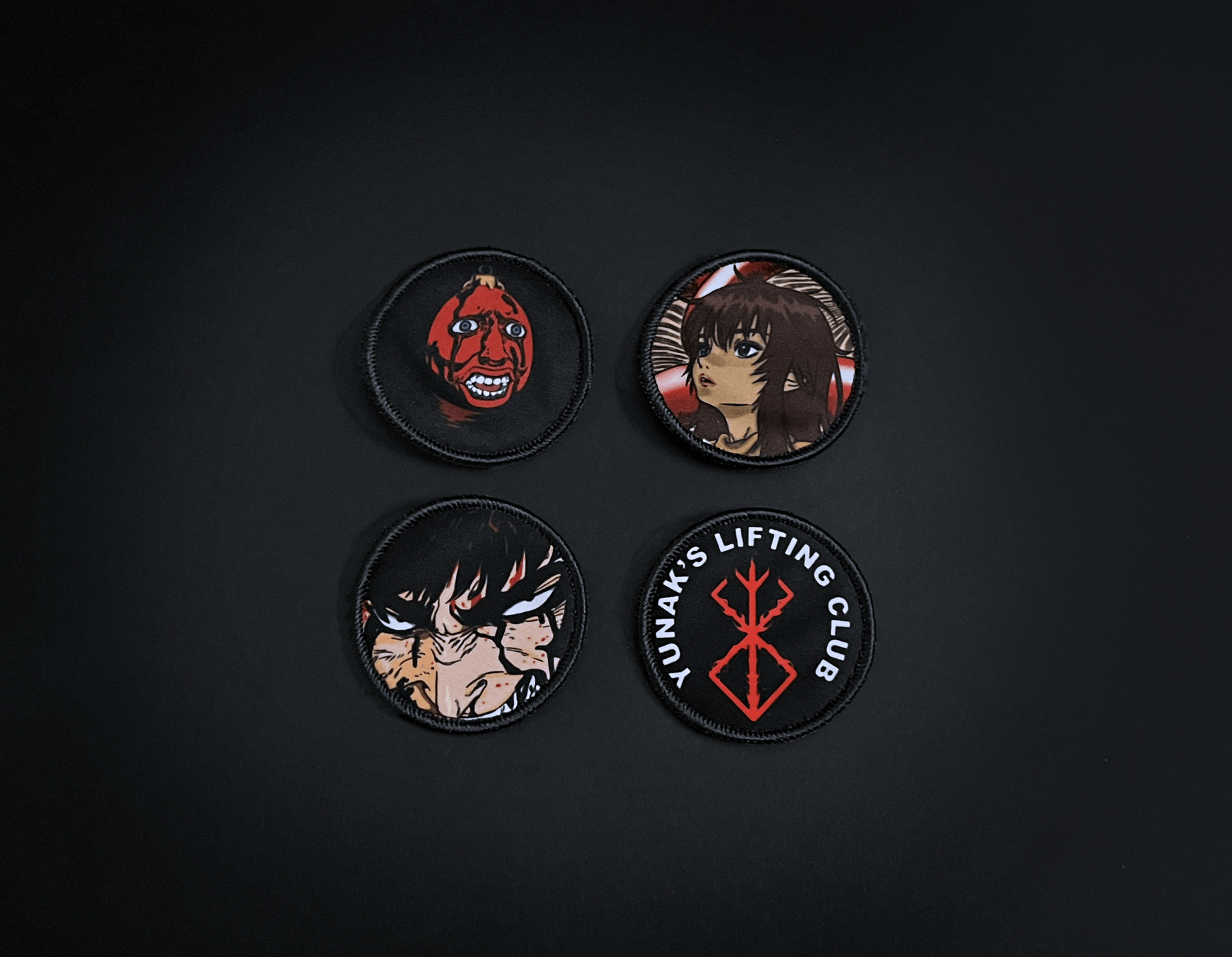 A photo of the 4 anime embroidery patches that come with this belt variation. First patch is behelit. Second patch is Casca, third is featuring Guts and the fourth is a Yunak's Lifting Club patch. The photo is top down view of the patches.