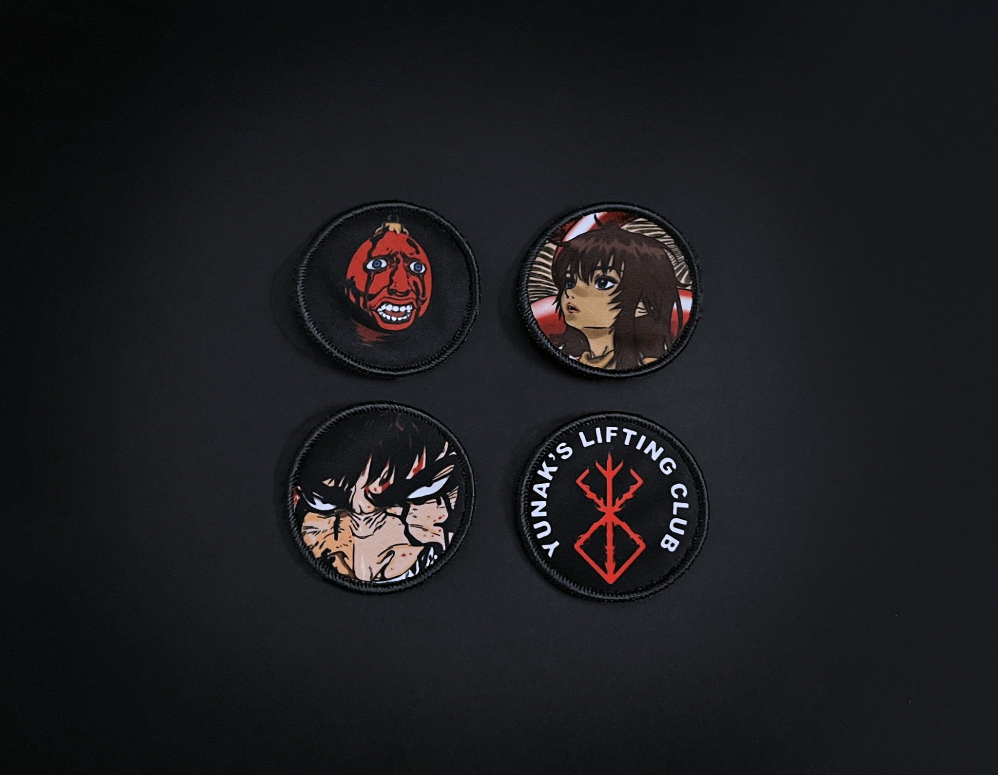 A photo of the 4 anime embroidery patches that come with this belt variation. First patch is behelit. Second patch is Casca, third is featuring Guts and the fourth is a Yunak's Lifting Club patch. The photo is top down view of the patches.