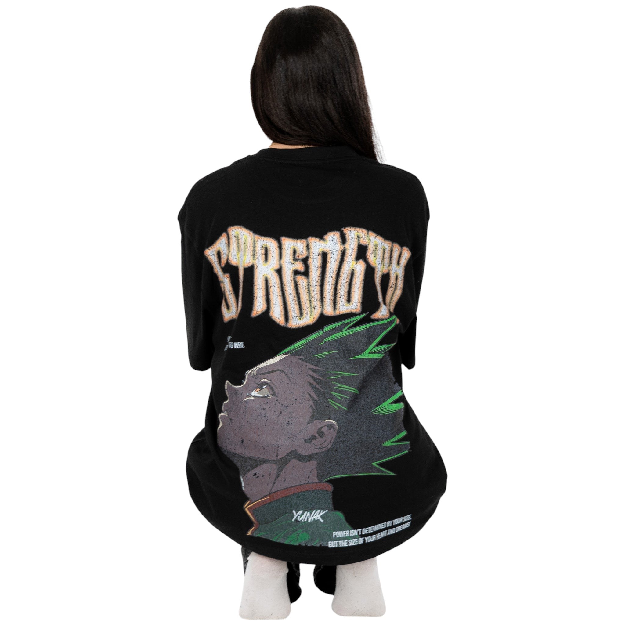 Person wearing a black t-shirt with graphic design of Gon from HunterxHunter on the back, squatting against a white background
